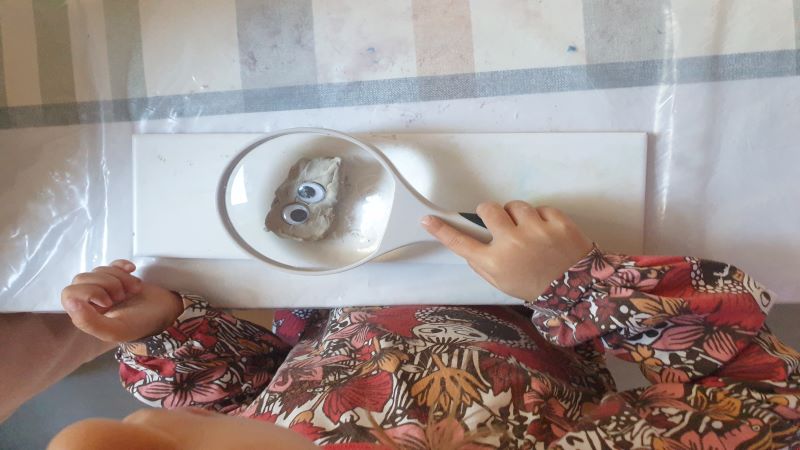 Barn som tittar på en lerfigur med ett förstoringsglas